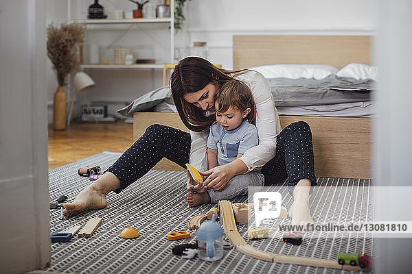 Mutter und Sohn spielen mit Spielzeug auf dem Teppich im Schlafzimmer