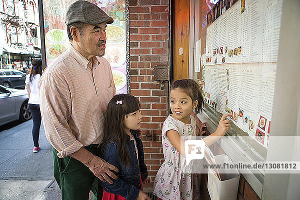 Mädchen zeigt Großvater und Schwester die Speisekarte  während sie gegen das Restaurant stehen