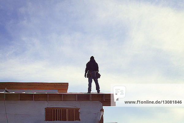 Niedrigwinkelansicht eines auf dem Dachbalken stehenden Arbeiters an einem sonnigen Tag