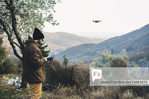 Seitenansicht eines männlichen Wanderers  der einen Quadcopter fliegt  während er auf einem Berg vor klarem Himmel steht
