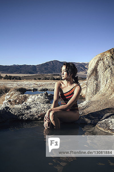 Nachdenkliche Frau sitzt auf einem Felsen in Bridgeport Hot Springs vor strahlend blauem Himmel