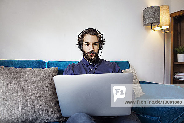 Businessman wearing headphones using laptop on sofa in office