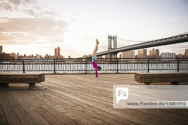 Woman doing handstand in promenade against Manhattan bridge