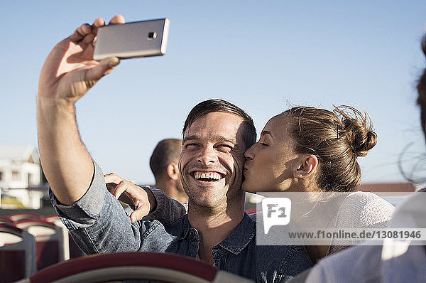 Happy man taking selfie while girlfriend kissing him in double-decker bus