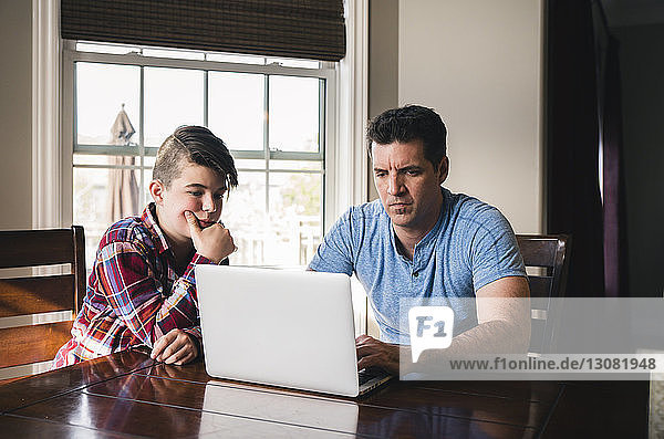Son looking at father using laptop computer at home