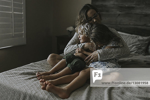 Frau umarmt Kinder  während sie auf dem Bett sitzt