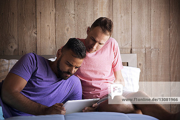 Homosexuelles Paar benutzt einen Tablet-Computer  während es auf dem Bett im Resort liegt