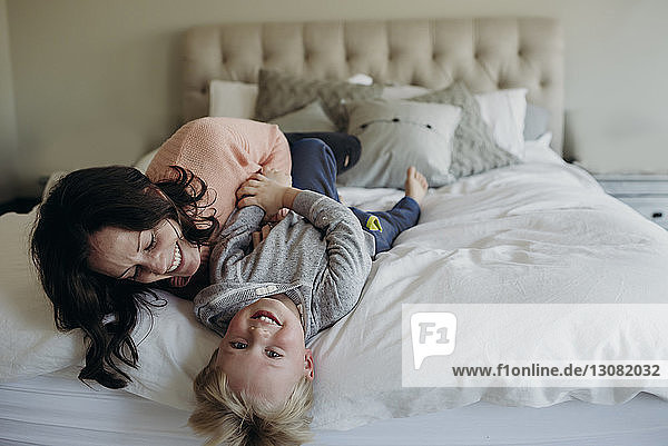 High angle view of happy mother playing with son while lying on bed at home