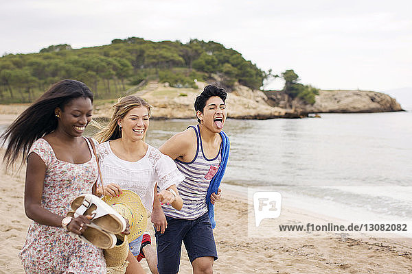 Cheerful friends running on beach during vacation