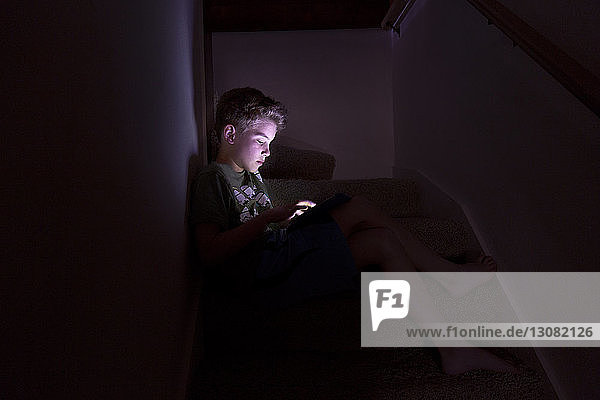 Junge spielt ein Spiel auf einem Tablet-Computer  während er zu Hause auf einer Treppe sitzt