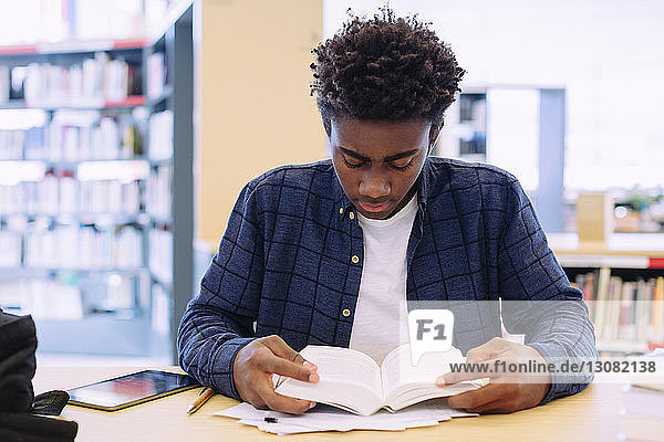 Mann liest Buch  während er in der Bibliothek am Tisch sitzt