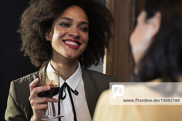 Smiling woman talking to friend while having wine at home