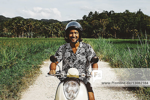 Porträt eines lächelnden Motorrad fahrenden Mannes auf unbefestigter Straße gegen den Himmel