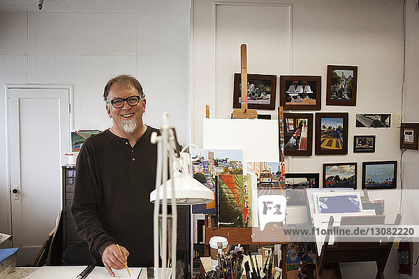 Portrait of smiling painter standing at table in workshop