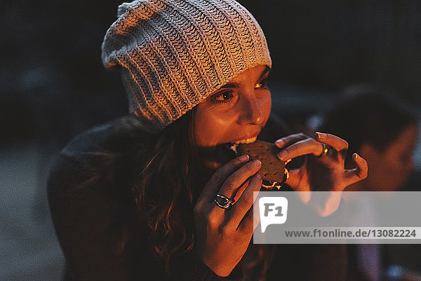 Woman eating smore while sitting in backyard at night