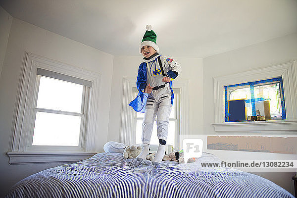 Glücklicher Junge  der zu Hause ein Kostüm trägt und auf dem Bett hüpft