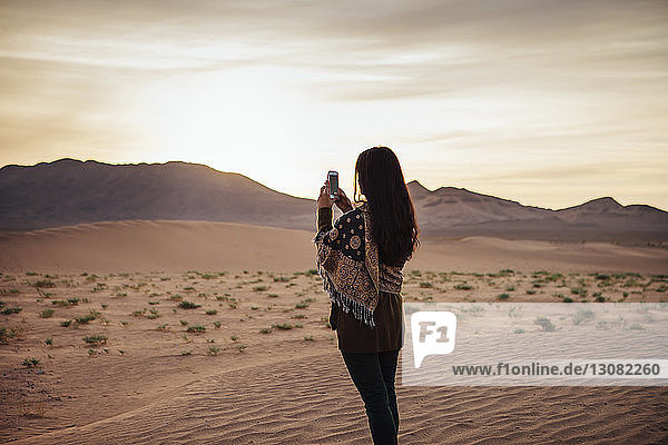 Frau fotografiert per Handy in der Wüste vor bewölktem Himmel