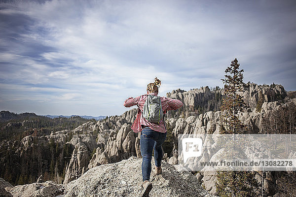 Rear view of woman jumping on rock against mountains and sky