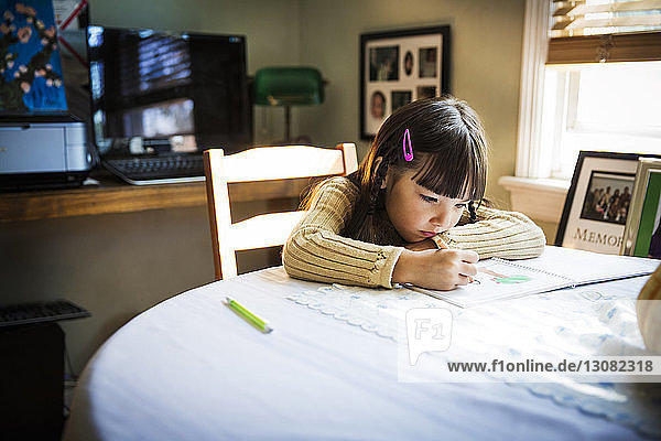 Girl drawing on book while sitting at table
