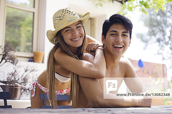 Porträt einer glücklichen Frau im Bikini  die sich an einen am Tisch sitzenden Mann ohne Hemd lehnt