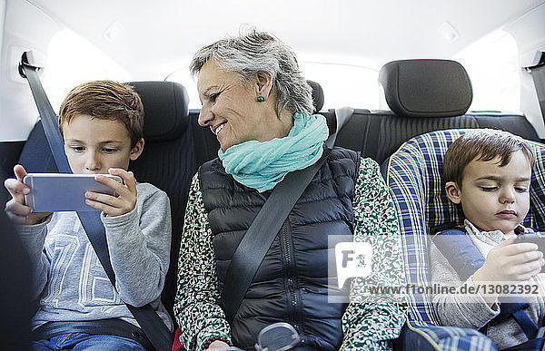Ältere Frau sieht ihren Enkel an  der im Auto ein Smartphone benutzt