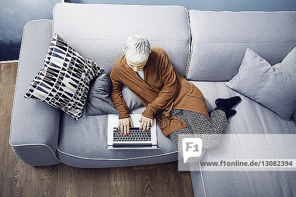 Woman using laptop while relaxing on sofa at home