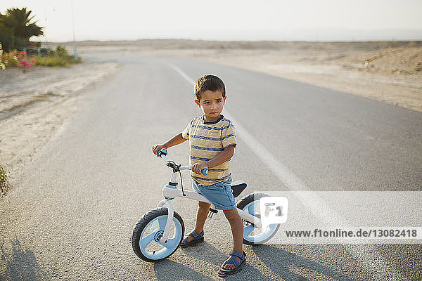 Junge in voller Länge mit Fahrrad  der auf der Landstraße stehend wegschaut