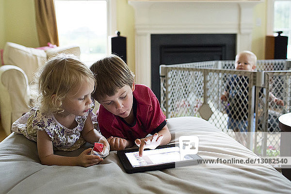 Kleiner Junge schaut Geschwistern am Tablet-Computer zu  während er in der Krippe steht