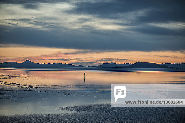 Silhouette person standing on Bonneville Salt Flats against cloudy sky