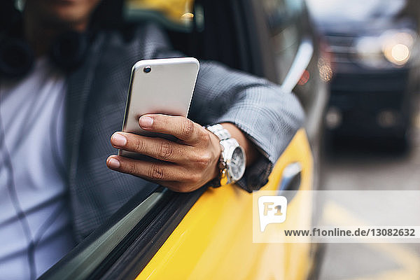 Midsection of businessman using smart phone while sitting in taxi