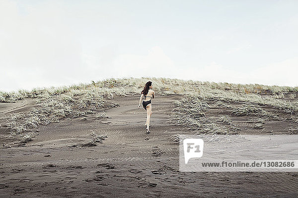 Rückansicht einer Frau  die auf nassem Sand am Bethells Beach vor klarem Himmel läuft