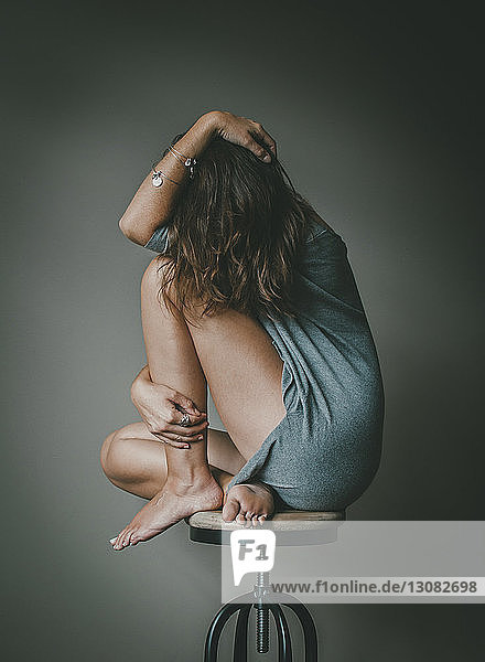 Full length of depressed woman with obscured face sitting on stool against wall