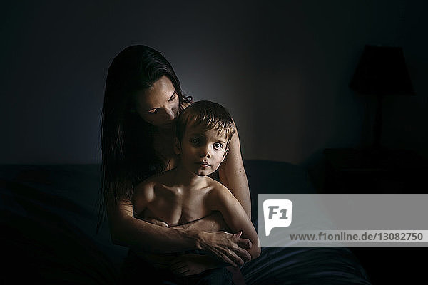 Portrait of boy with mother sitting on bed at home