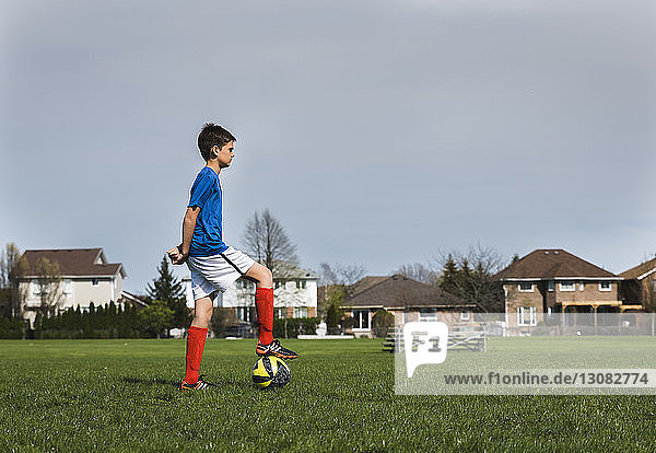 Seitenansicht eines Jungen mit Fussball  der auf einem Rasenfeld steht
