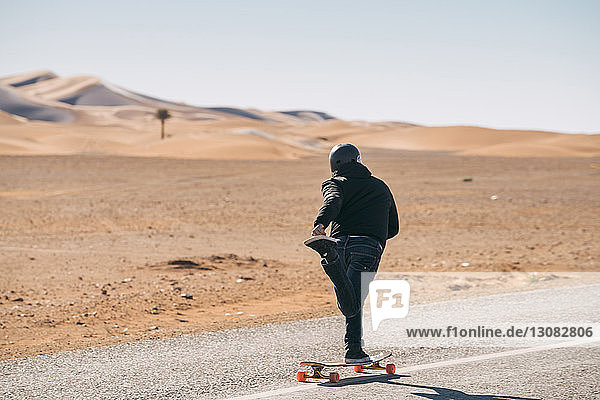 Full length rear view of man skateboarding on road against sky