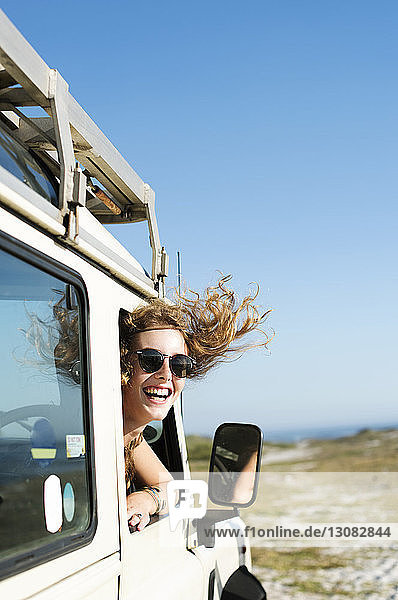 Glückliche Frau mit Sonnenbrille  die am sonnigen Tag durch das Autofenster schaut