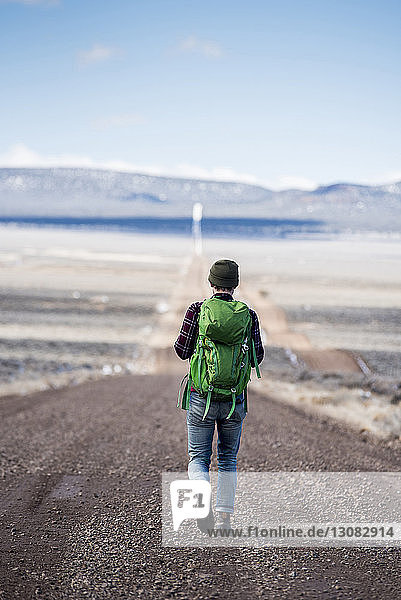 Rückansicht eines Wanderers mit grünem Rucksack beim Wandern in der Wüste