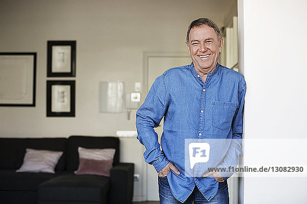 Portrait of happy senior man standing with hands in pockets at home