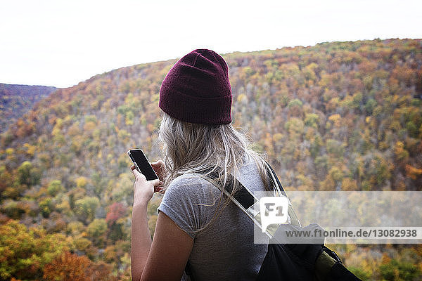 Rear view of young woman using phone while standing against mountain