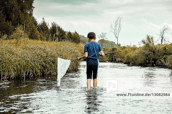 Rear view of boy holding butterfly fishing net while standing in lake