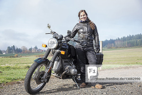 Ganzfigur einer Motorradfahrerin in Lederjacke  die mit dem Motorrad auf unbefestigter Straße steht