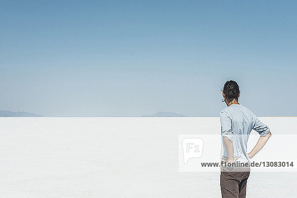 Rear view of man standing at salt flat against clear blue sky