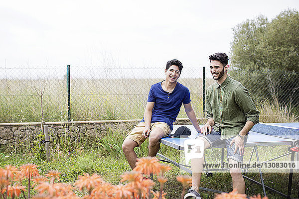 Happy male friends sitting on tennis table at yard