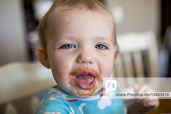 Portrait of cute baby girl with messy mouth sitting at home