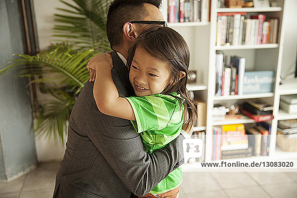 Lächelnde Tochter umarmt Vater  während sie zu Hause im Wohnzimmer steht