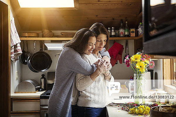 Glückliche Tochter umarmt Mutter  während sie in der Küche steht