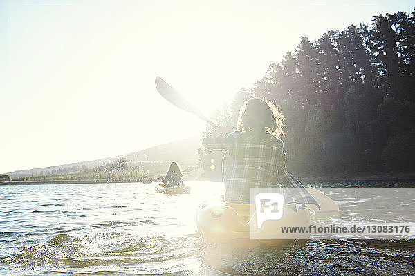 Rückansicht von Freundinnen  die bei Sonnenschein auf dem See Kajak fahren