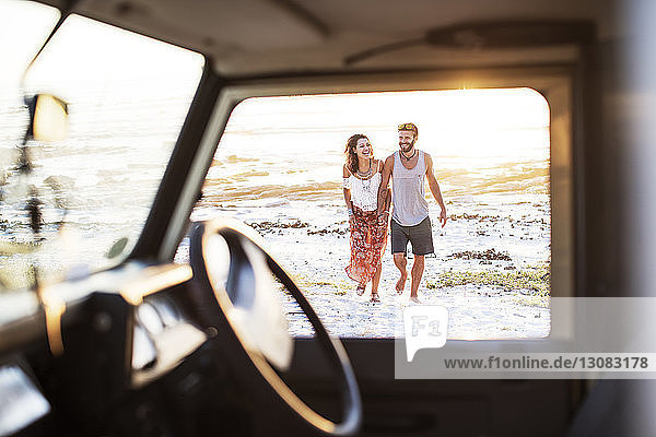 Cheerful couple walking at beach seen through window of off-road vehicle