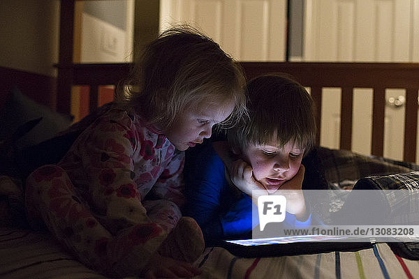 Siblings using tablet computer on bed at home