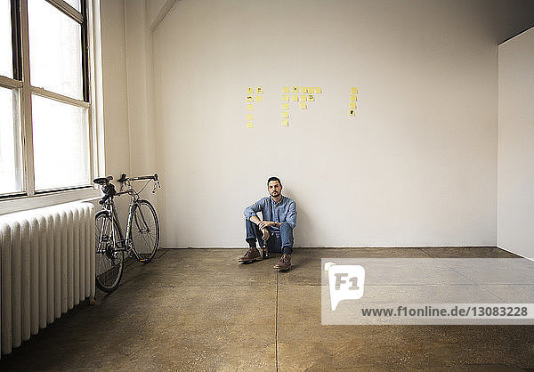 Full length of businessman sitting against wall with sticky notes in creative office